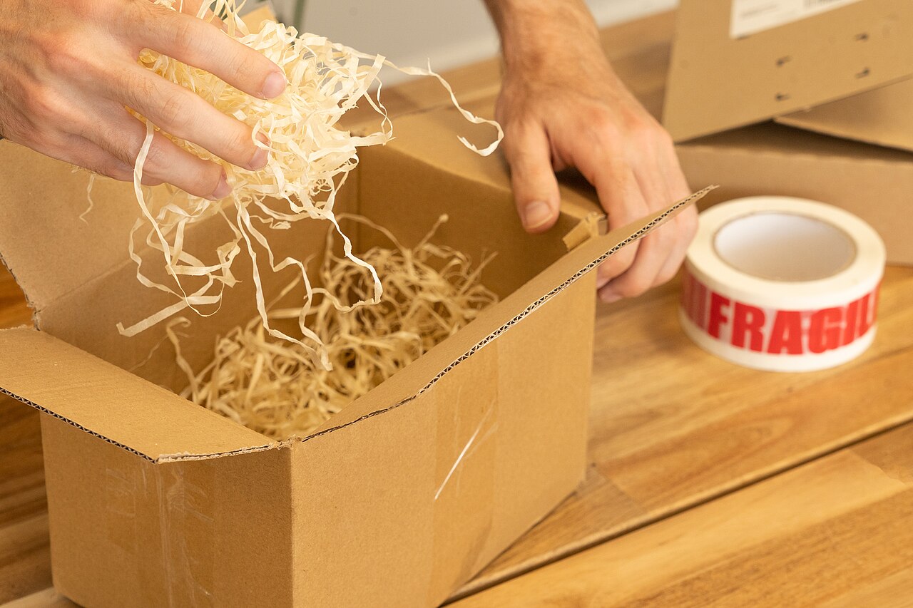 Zwei Hände polstern einen Versandkarton mit Holzwolle aus